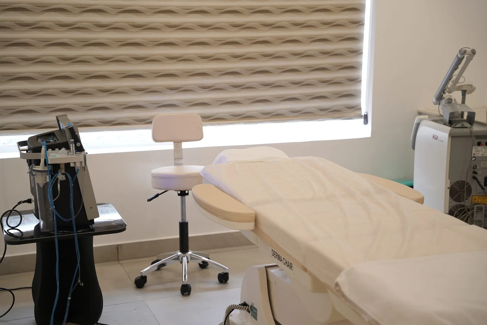 A treatment room with a derma chair, stool and clinical equipment beside a bright window